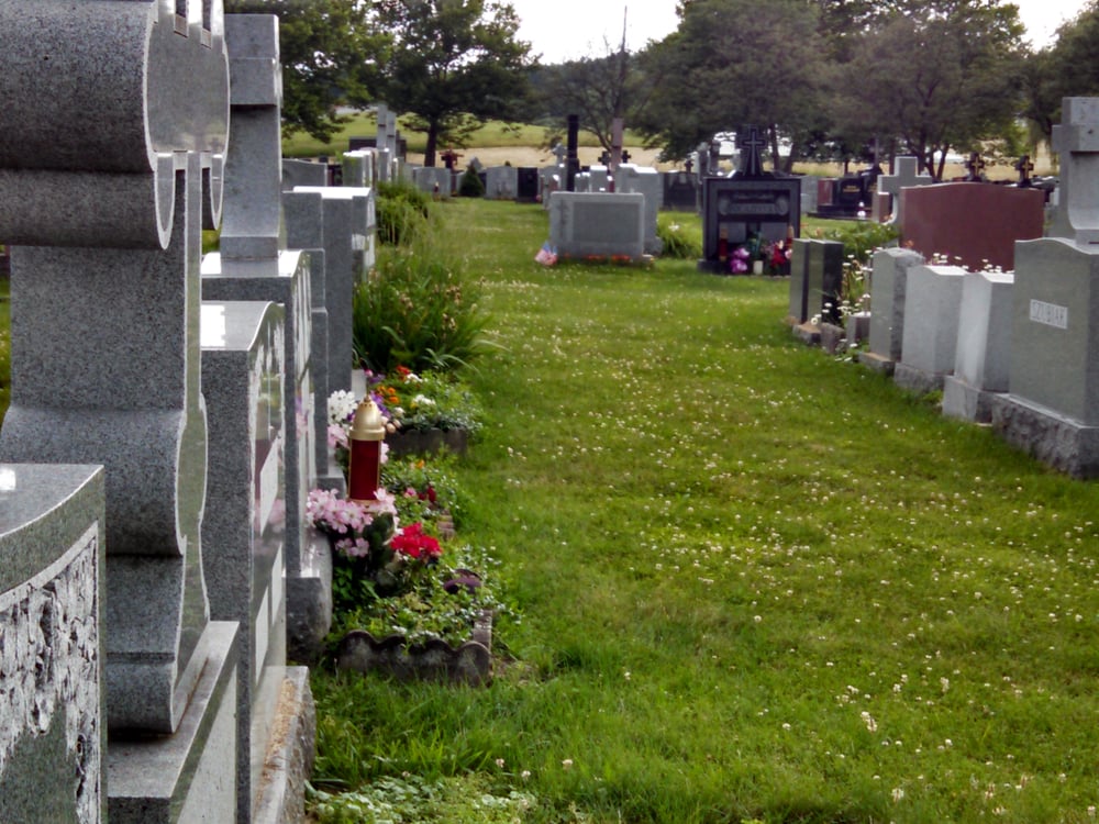 A row of granite monuments standing in a cemetery with flowers and a grave lantern at their bases