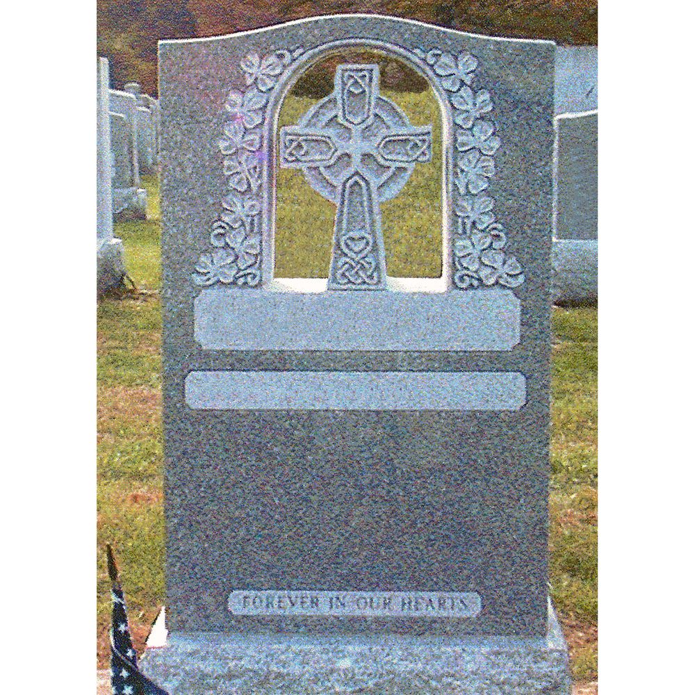 Upright grey granite monument with a carved Celtic ring cross set in an arch, framed by a shamrock border